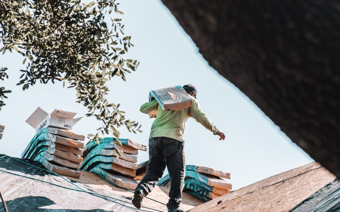 Man on a roof carrying roofing supplies