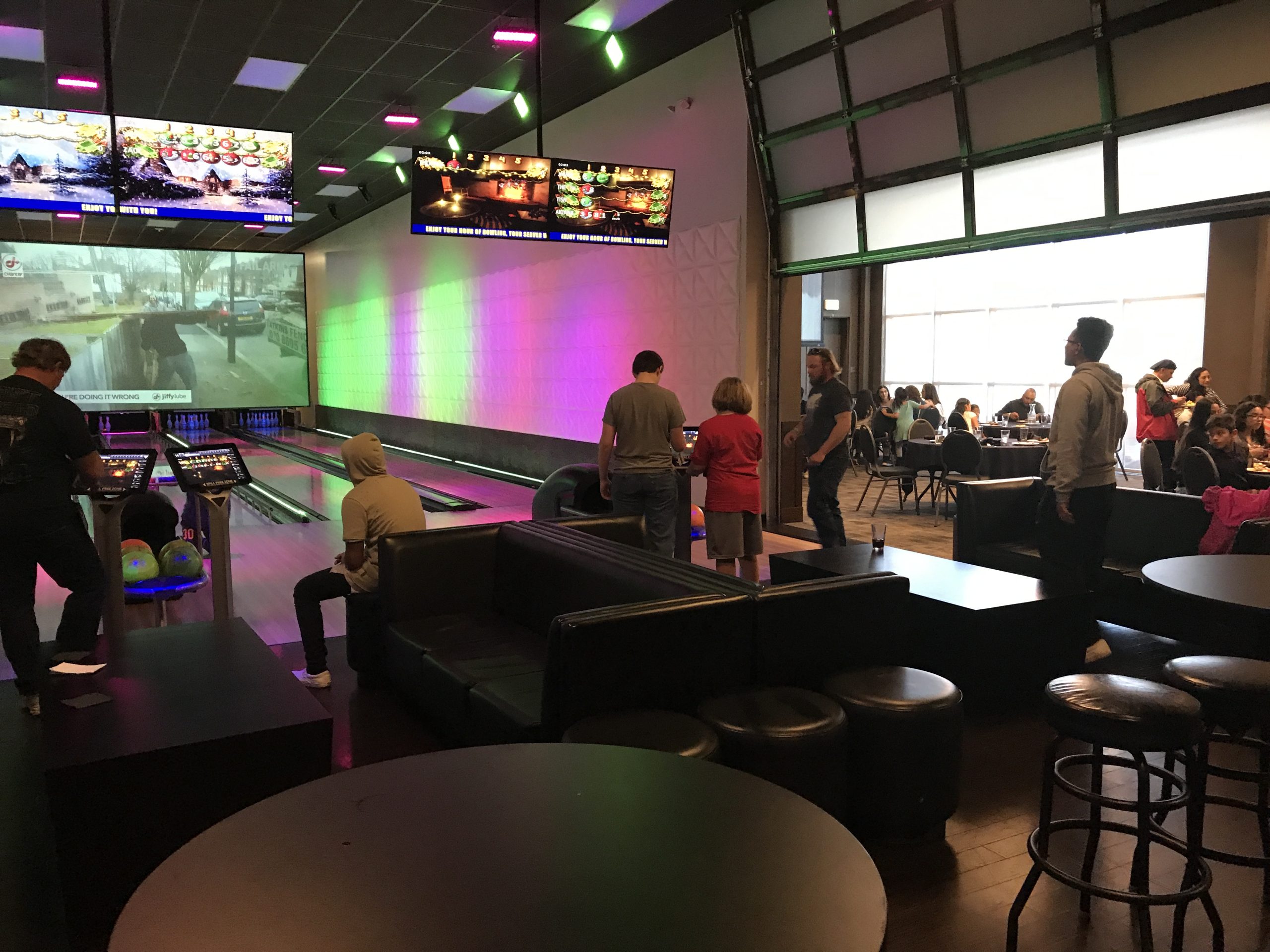 A bowling alley with people watching tvs and bowling.