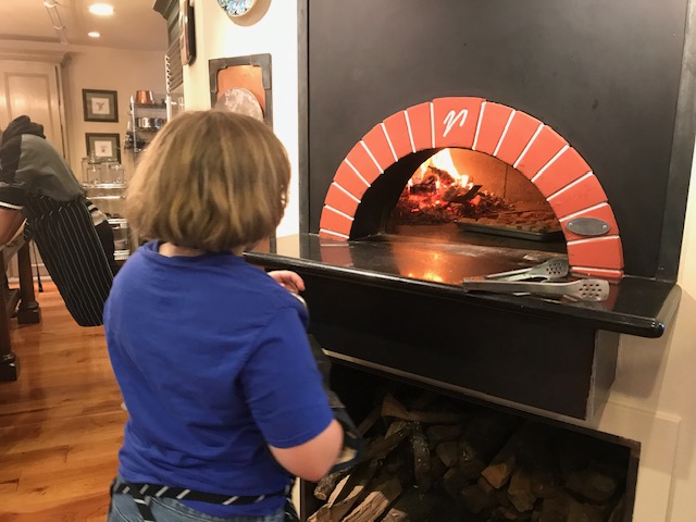 A child standing in front of an important pizza oven.