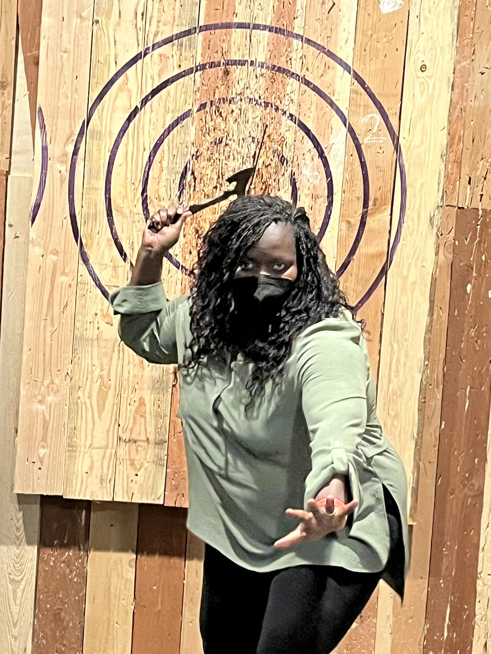 A woman wearing a mask in front of a wooden target.