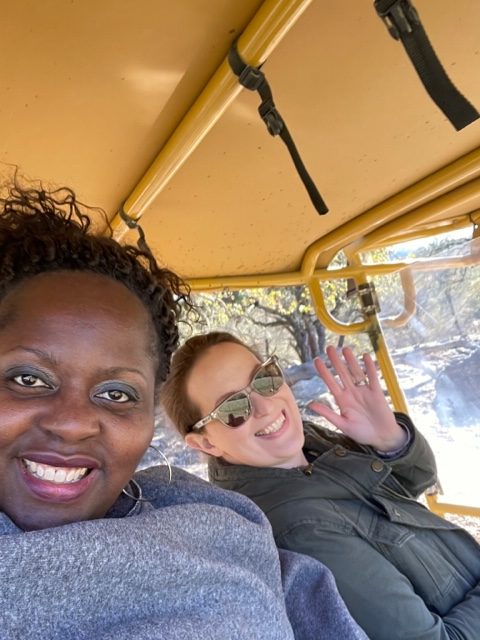 Two women in a safari vehicle waving at the camera.