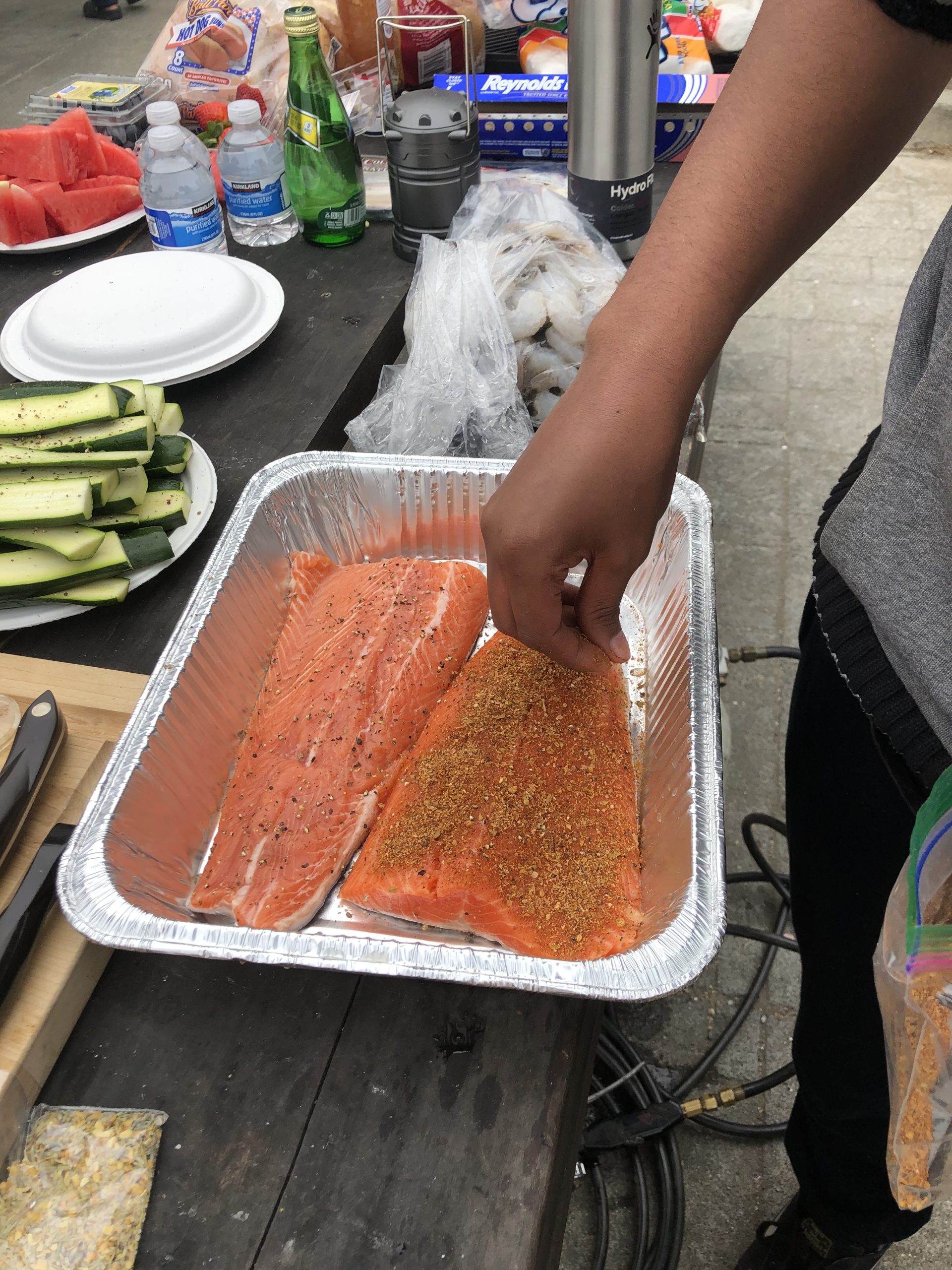 A person is putting seasoning on a piece of salmon.