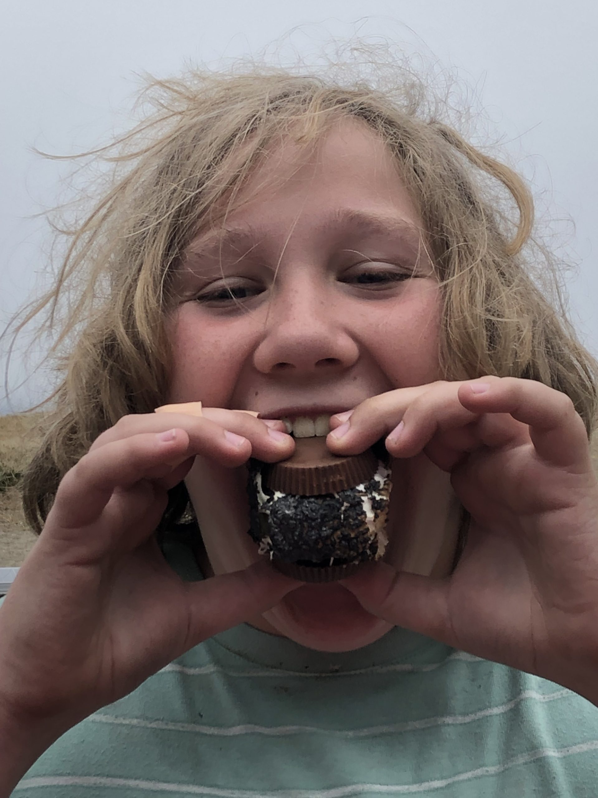 A young girl is holding a chocolate donut in her mouth.