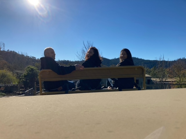 Three people sitting on a bench in the sun.